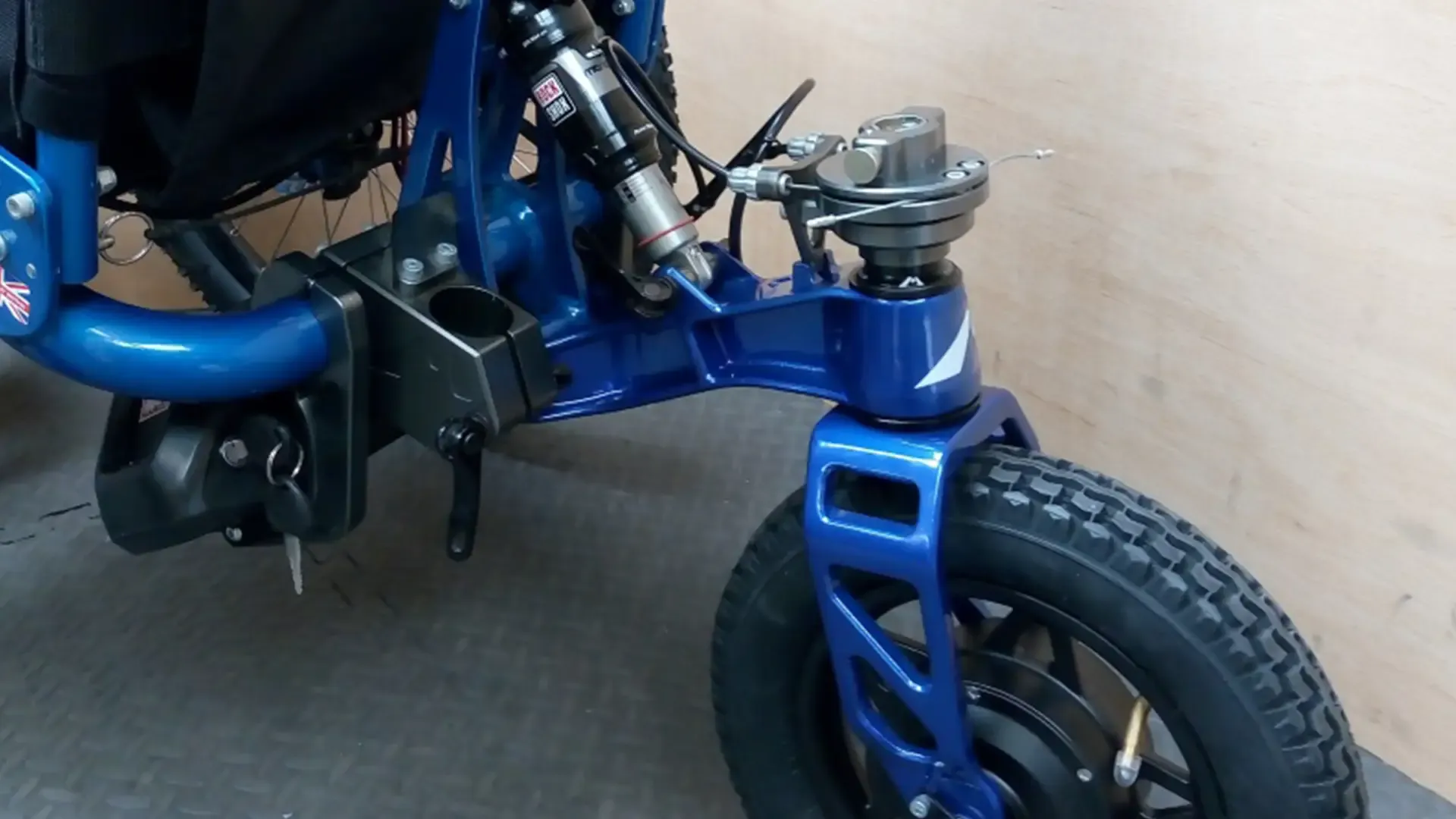 MOUNTAIN TRIKE E-KIT 5 Detailed close-up of blue wheelchair front wheel suspension, designed for outdoor access by disabled users, CIC community project.