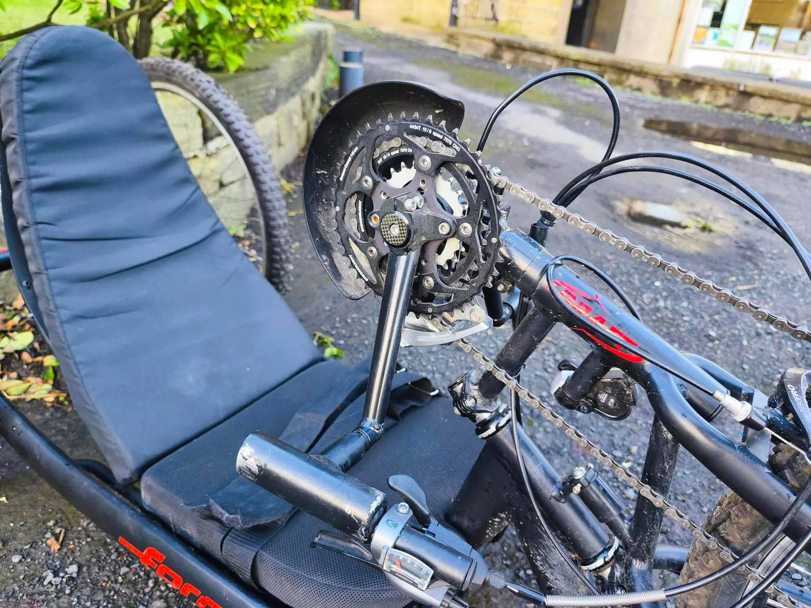 Recumbent handcycle for disabled access, outdoor adaptive cycling by not-for-profit near stone wall and bushes, inclusive green spaces.