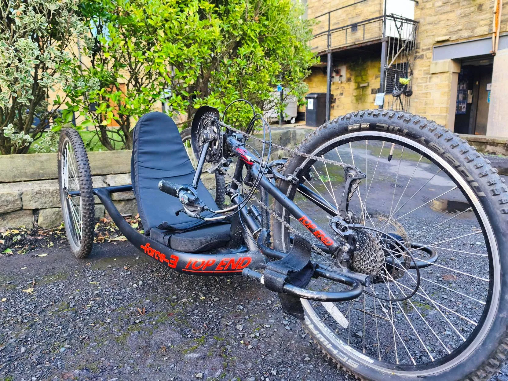 Accessible three-wheeled handcycle for disabled people on gravel path, promoting inclusive outdoor activities at our Community Interest Company.