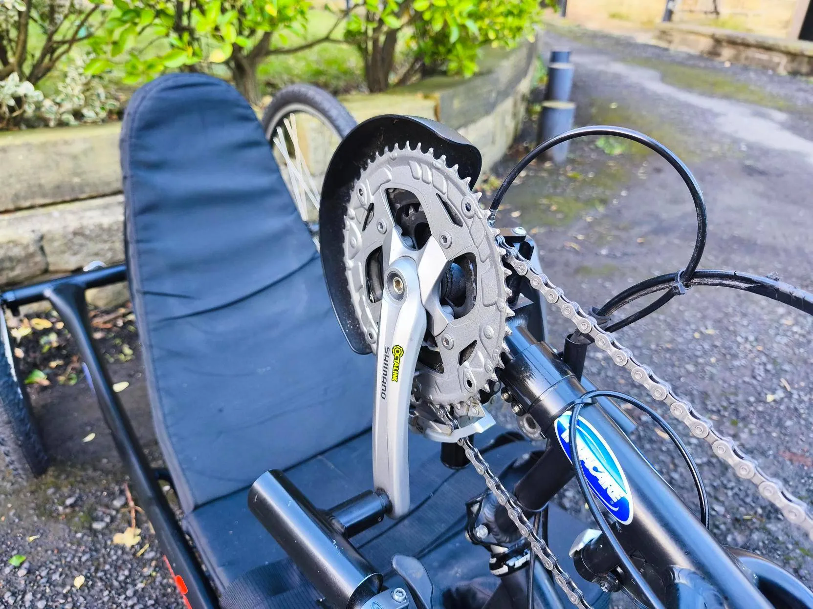 Recumbent tricycle gear and pedal close-up, padded seat, greenery—accessible cycling for disabled people by our not-for-profit CIC.